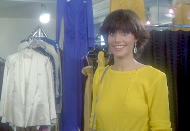 it’s giving dork (lovingly) Lorraine Bracco smiling in a yellow top inside a clothing boutique scene from her early acting role in the 1979 French film Duos sur canapé.