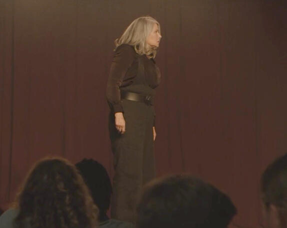 it’s giving S2 disappointed Melfi in the diner. Lorraine Bracco on a stage in dark clothing seen from the audience in Monster Summer.