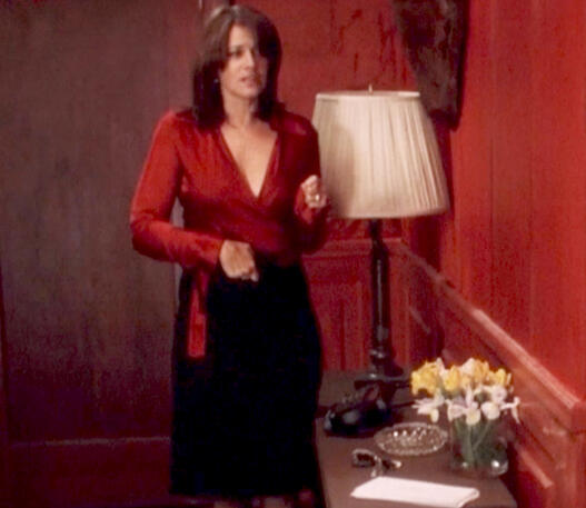 5 Lorraine Bracco in a red satin blouse and black skirt standing with her phone to her stomach in Crazy for Love.