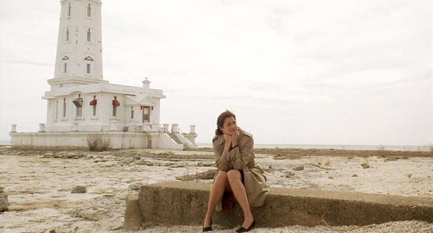 9 Lorraine Bracco sitting happily on a concrete wall near a beach lighthouse in Custody of the Heart.