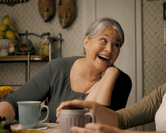 3 Lorraine Bracco laughing happily at a table in film The Mother, the Menacer, and Me.