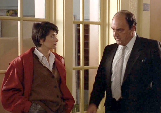 4 Lorraine Bracco and a man in a suit talking in a hallway scene from the movie Sing 1989.