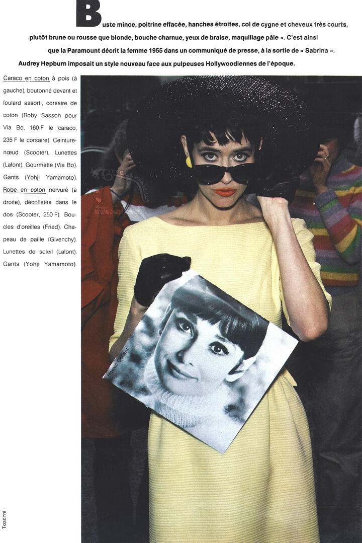Continuation of Elle magazine spread. Lorraine Bracco wears a boatneck yellow dress, a large black wide-brimmed hat, sunglasses, and black gloves while presenting a black and white headshot photo of Audrey Hepburn.